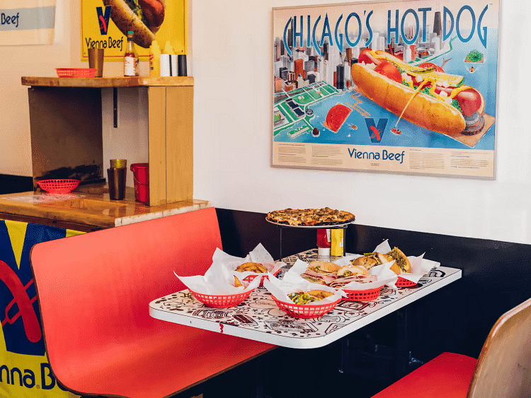 Diner with a table of hotdogs and fries, Vienna Beef signs, and a "Chicago's Hot Dog" poster.