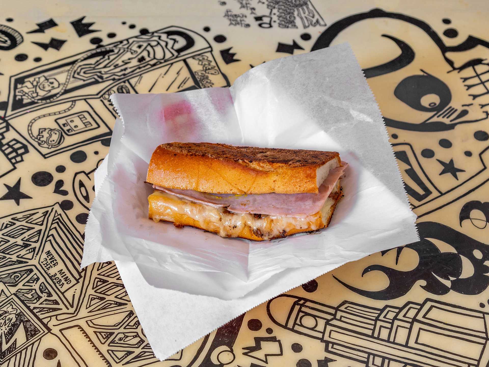 Grilled ham and cheese sandwich on parchment paper over a doodle-covered tablecloth.