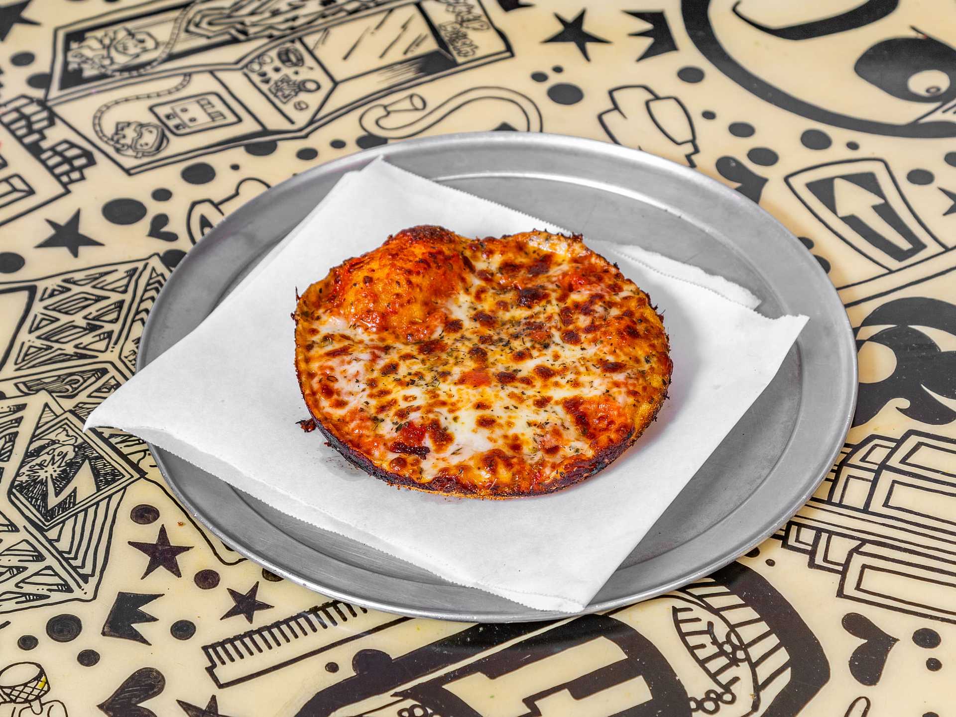 Cheese and pepperoni mini pizza on a silver plate with paper liner, placed on a patterned table.