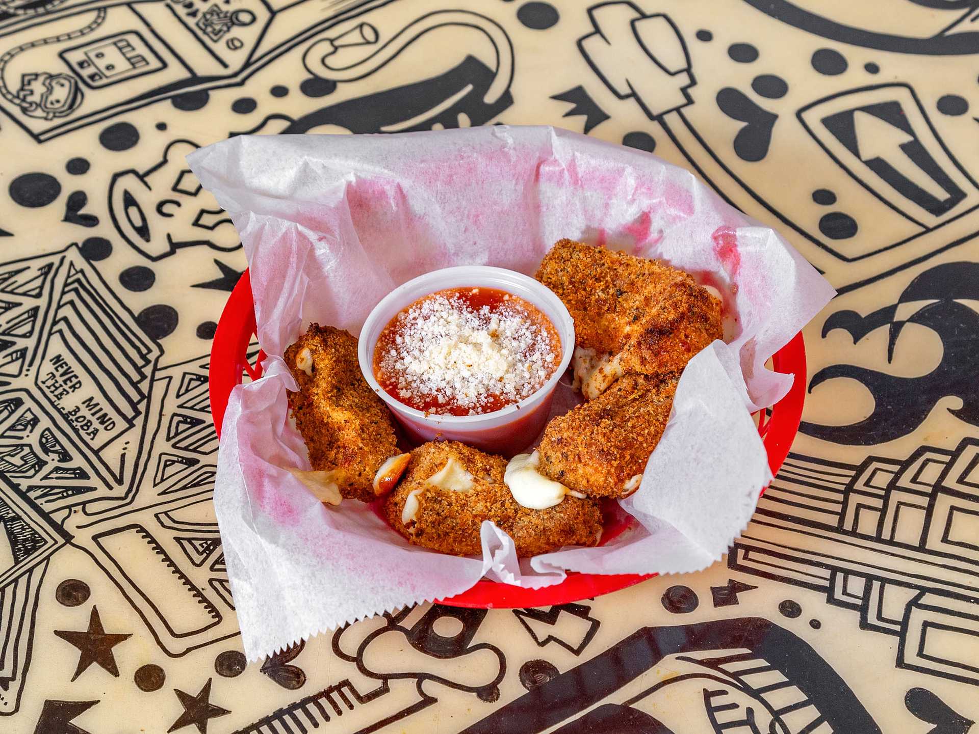 Basket of seasoned mozzarella sticks with marinara sauce, on a decorative table.